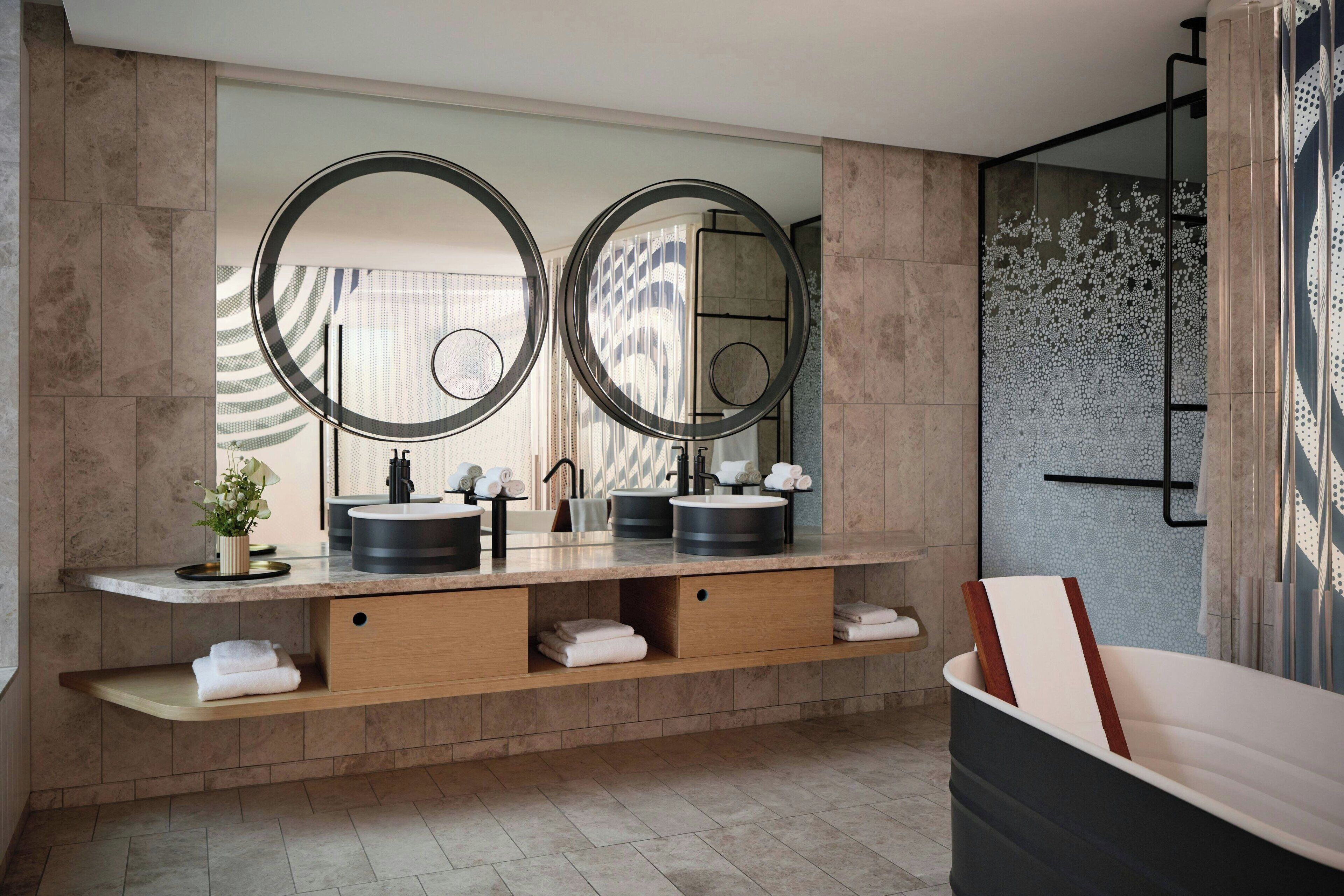 A modern bathroom with two sinks, a large mirror, and a bathtub.
