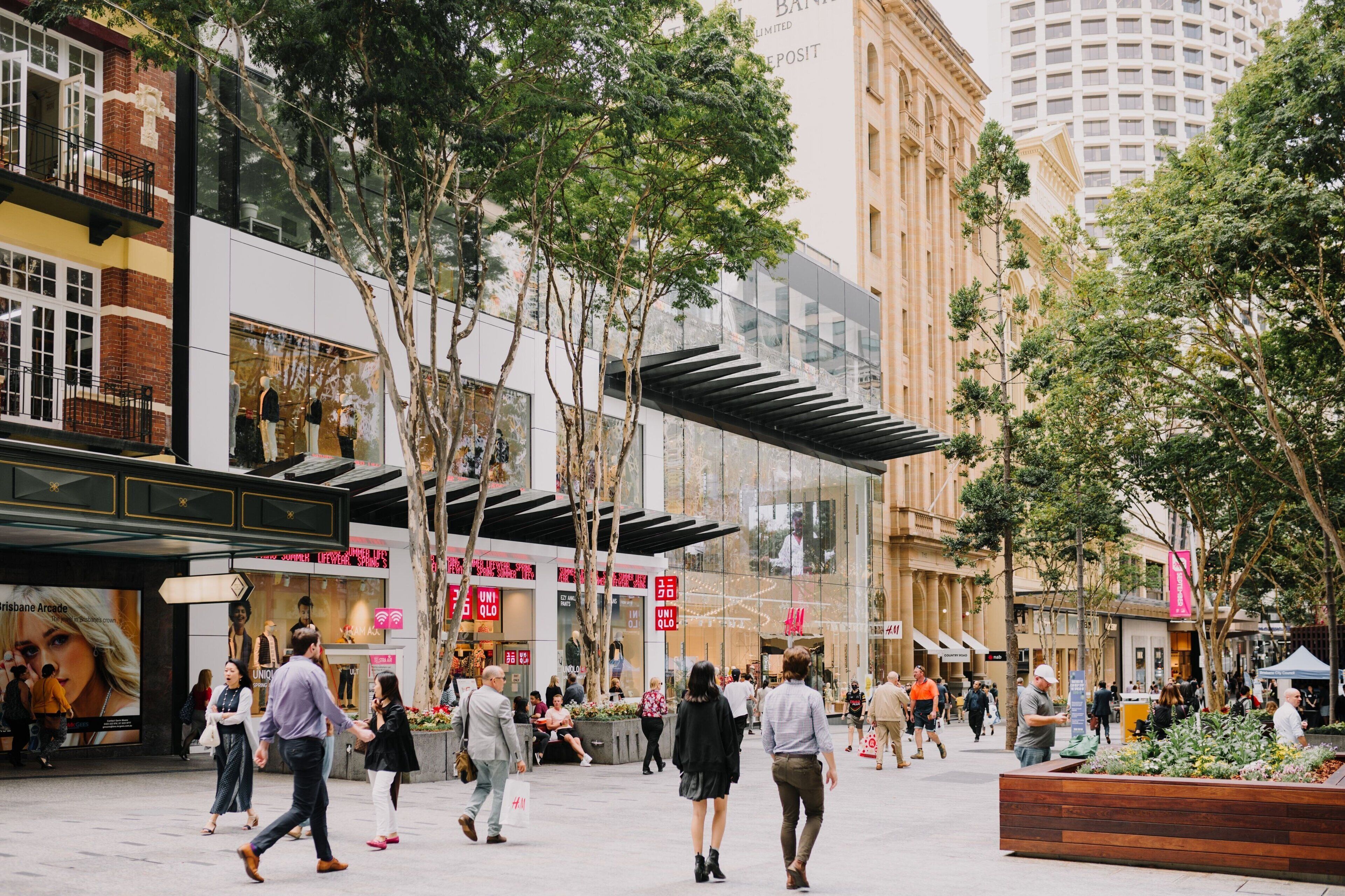 A busy urban shopping area with modern buildings, outdoor seating, and pedestrian traffic.