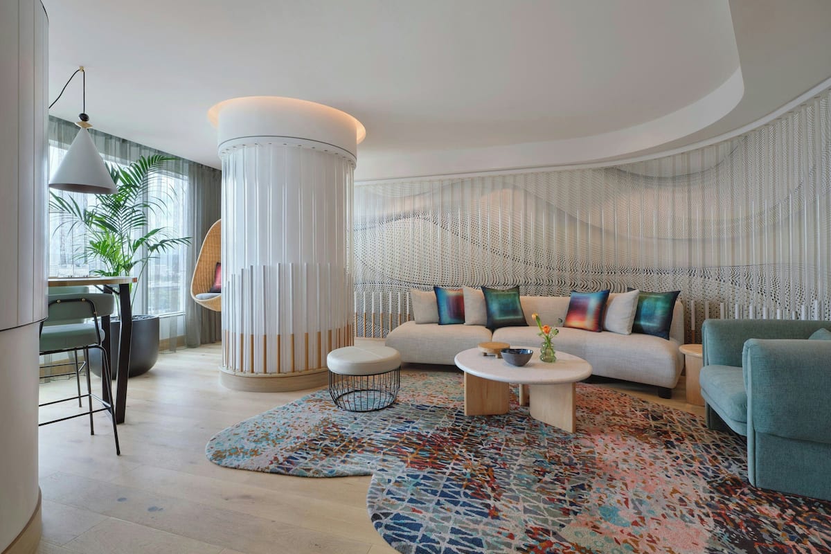 Un salon moderne avec une table basse ronde, un canapé agrémenté de coussins colorés, une grande colonne blanche et un tapis à motifs.