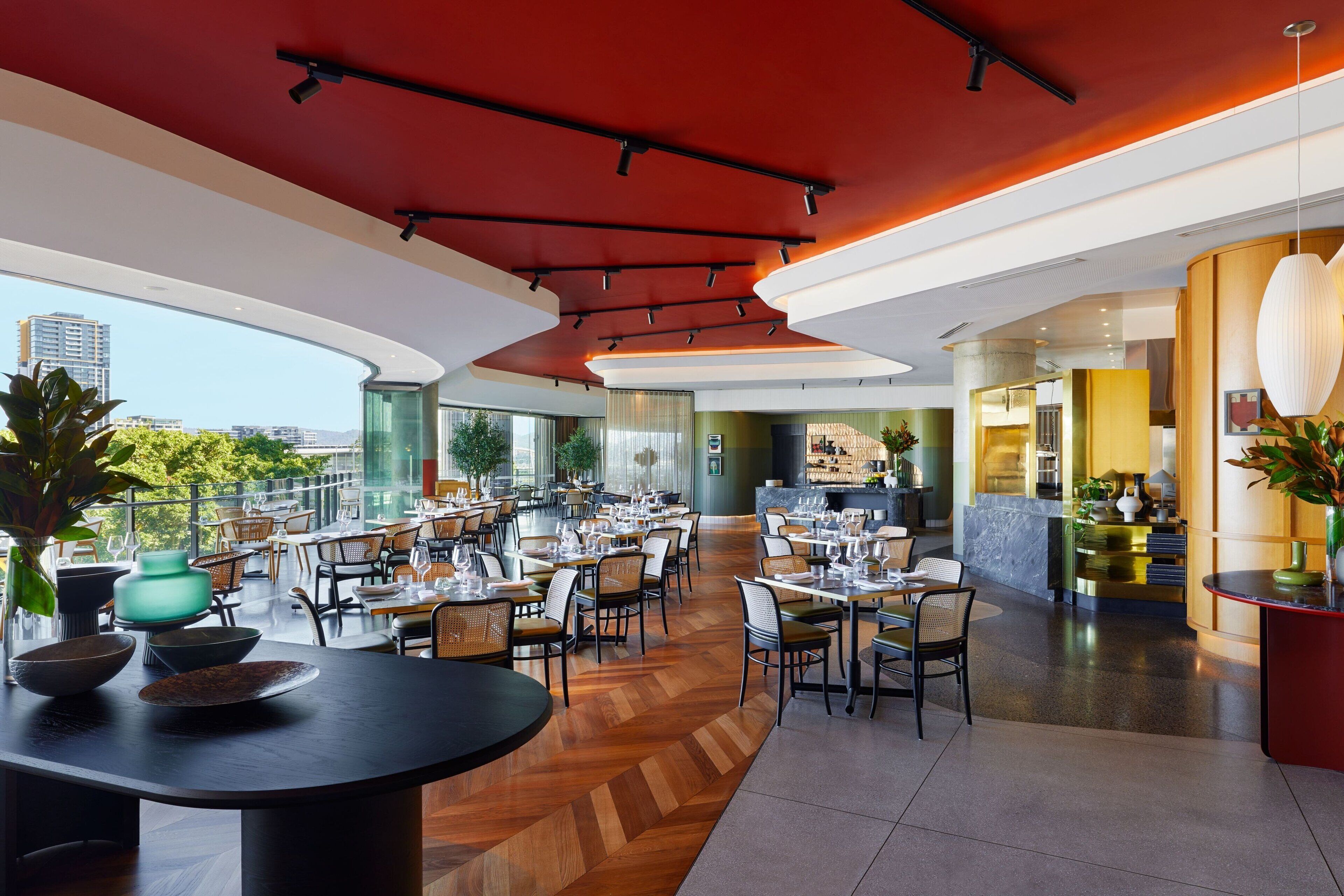A modern restaurant with a high ceiling, large windows, and a mix of seating arrangements.