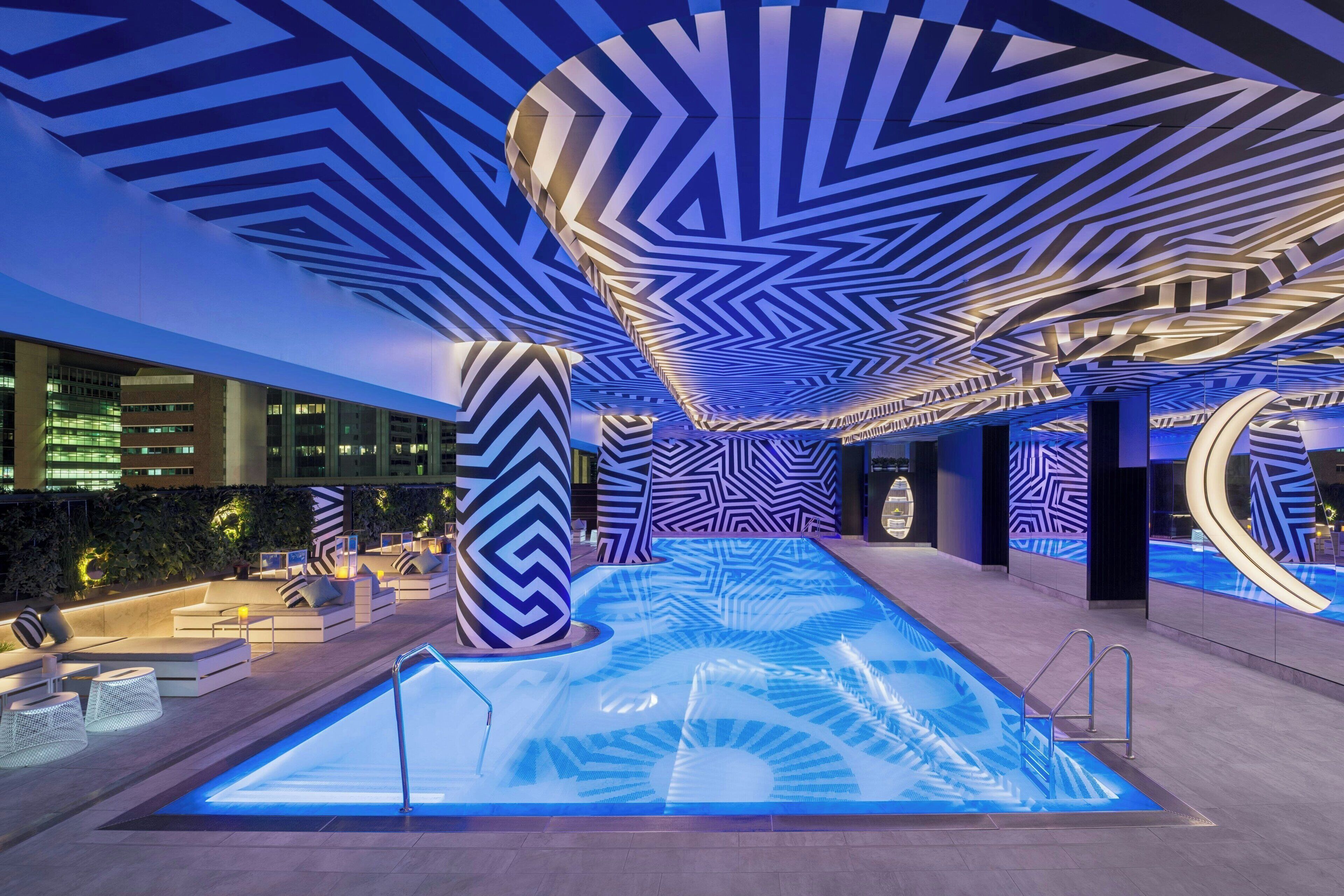 Un'area piscina interna moderna con motivi geometrici al soffitto e sedute relax.