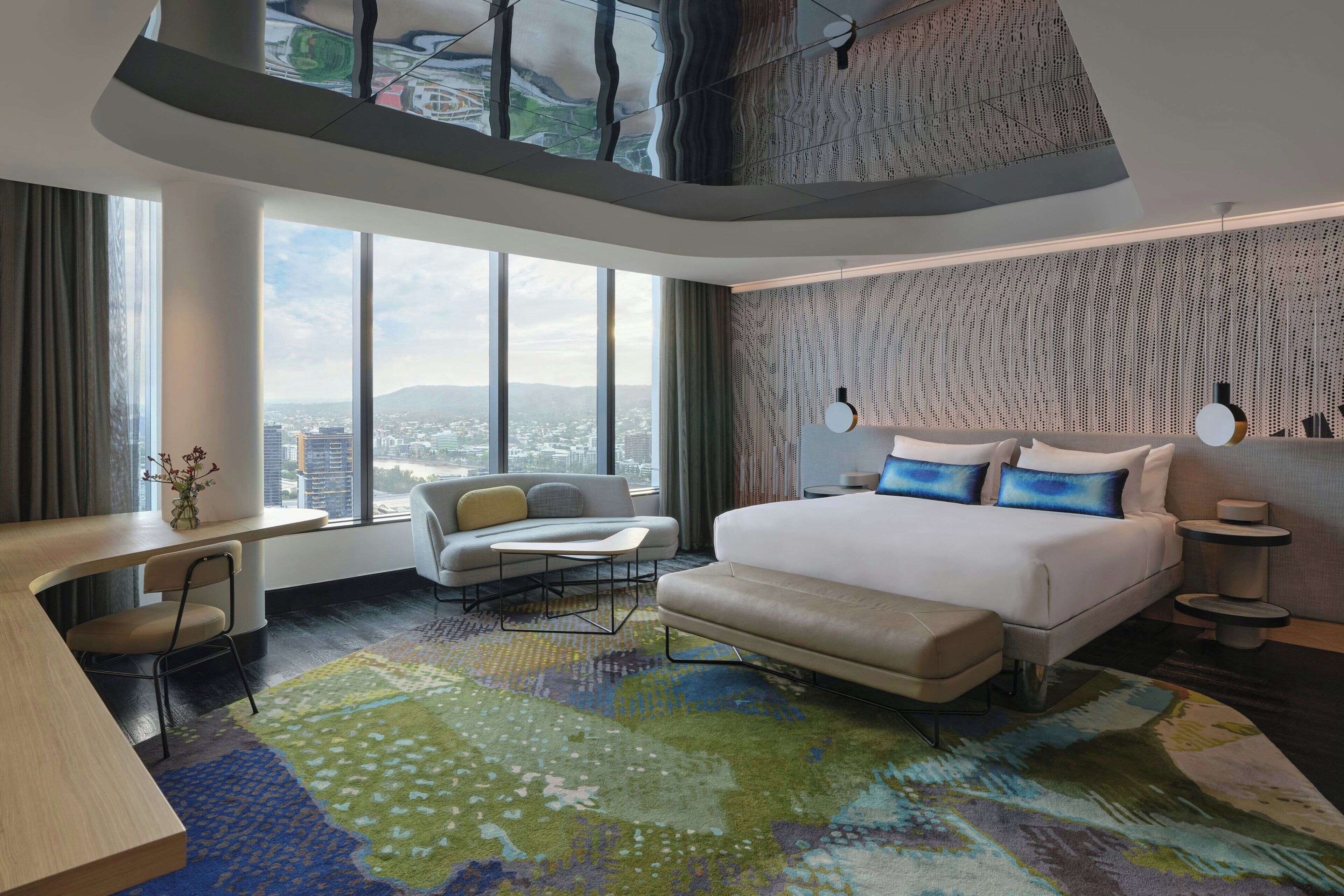 A modern hotel room with a large bed, a sofa, a desk, and a view of the city.