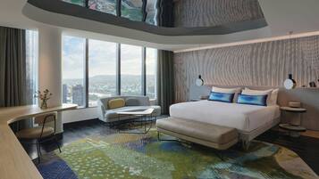 A modern hotel room with a large bed, a sofa, a desk, and a view of the city.