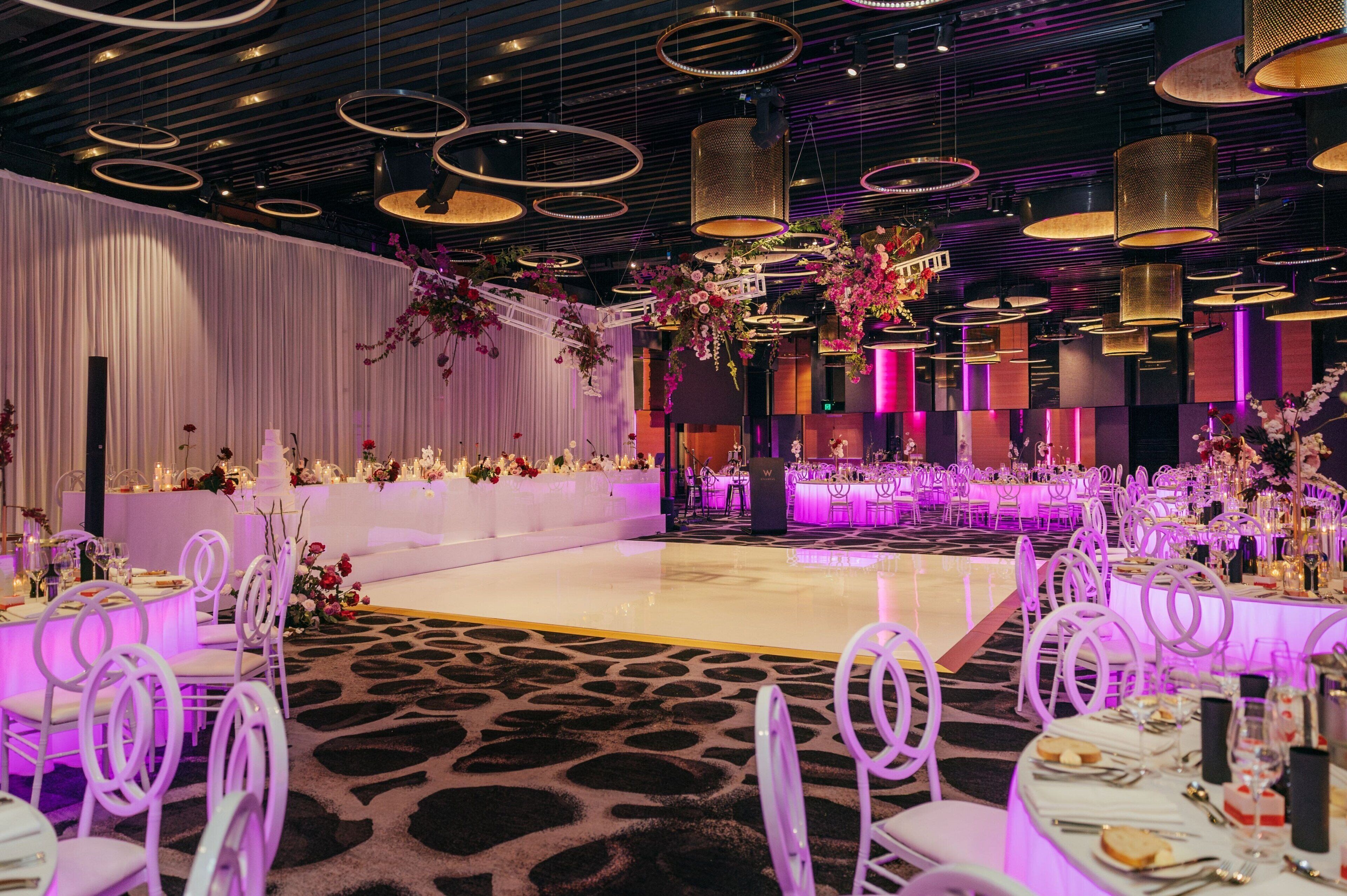 A banquet hall with round tables, white chairs, and purple lighting.