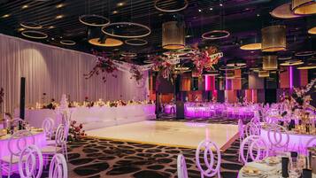 A banquet hall with round tables, white chairs, and purple lighting.