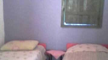 Quarto com duas camas, uma mesa pequena e janela com persianas.