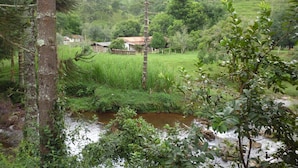 A rural landscape with a small house surrounded by lush greenery and a stream. - Apto 2 Férias na Fazenda Usina Térreo (Bocaina de Minas)