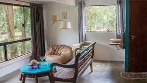 A room with a wooden bench, a table with drinks, a floor lamp, and a window with curtains. - Apto 2 Férias na Fazenda Usina Térreo (Bocaina de Minas)
