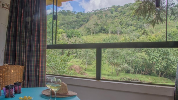 A room with a large window offering a view of a lush green landscape. - Apto 2 Férias na Fazenda Usina Térreo (Bocaina de Minas)