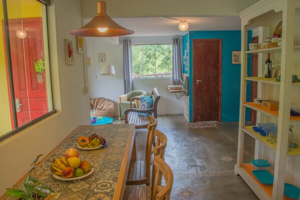 A dining area with a table set for two, a chair, a bookshelf, and a view of the outdoors.