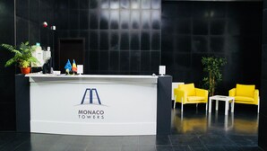 Un mostrador de recepción con un logotipo, dos plantas en macetas y dos sillas amarillas.
