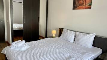 A neatly made bed with white bedding, a wooden wardrobe, a bedside lamp, and a framed picture on the wall.