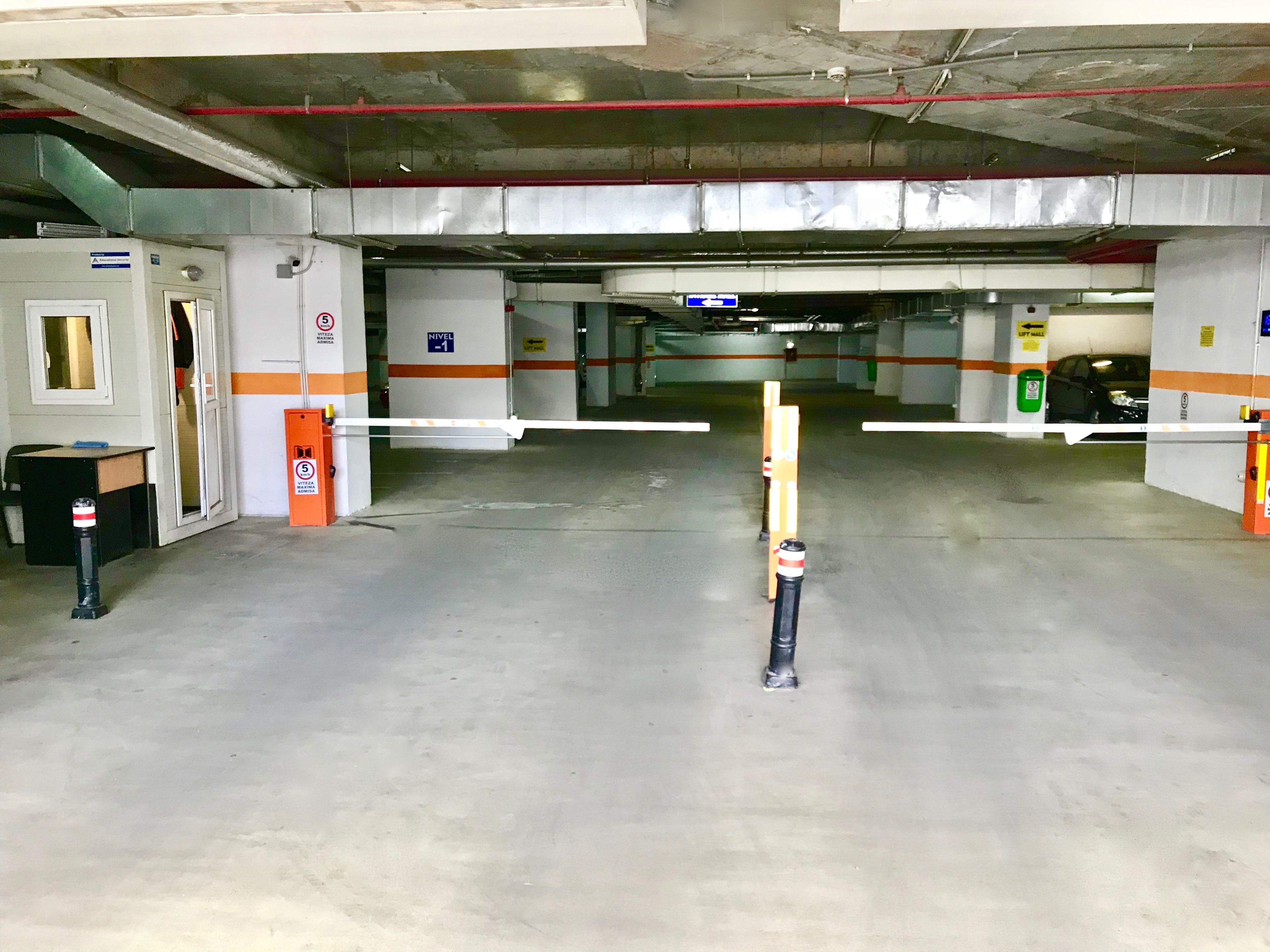 An underground parking garage with concrete floors, metal railings, and orange safety barriers.