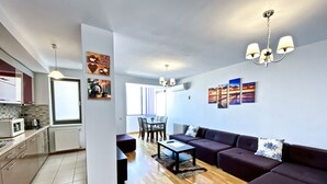 Un apartamento moderno con cocina, comedor y sala de estar. Cuenta con un juego de sofás, una mesa de comedor con sillas y una araña.