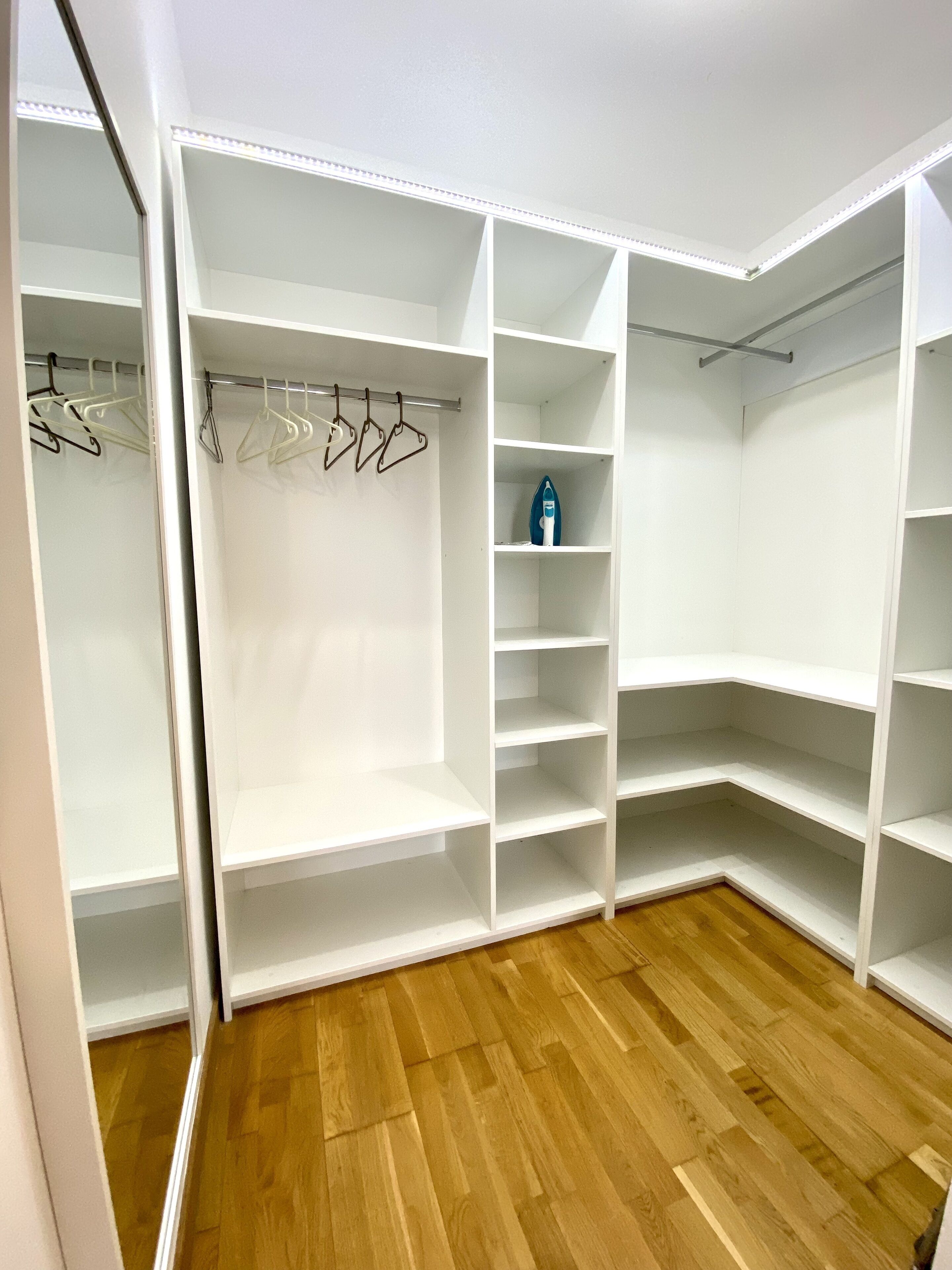 Un vestidor amplio con varias repisas y espacio para colgar, suelo de madera y paredes blancas.