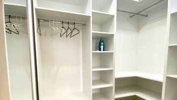 Un vestidor amplio con varias repisas y espacio para colgar, suelo de madera y paredes blancas.