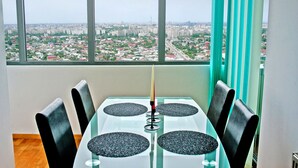 Un comedor con mesa y sillas, una vela y vistas de un paisaje urbano a través de amplios ventanales.