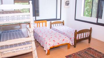 A room with bunk beds and two single beds, large windows, and a patterned rug.