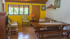 A room with a wooden ceiling, a bed with floral bedding, a table with benches, and a window with a view of greenery. - Apto 1 ferias na Fazenda Usina And. Sup. (Bocaina de Minas)