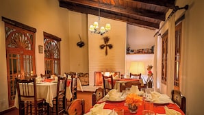 A dining area with wooden chairs and tables set for a meal, a chandelier, and a fireplace in the background. - Hotel El Patio de Monterrey (Independencia)
