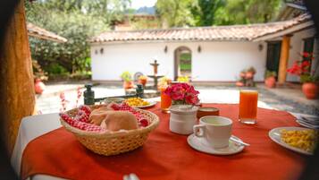 Una mesa de desayuno con una cesta de pan, una jarra de jugo de naranja, una taza de café y un plato de huevos.