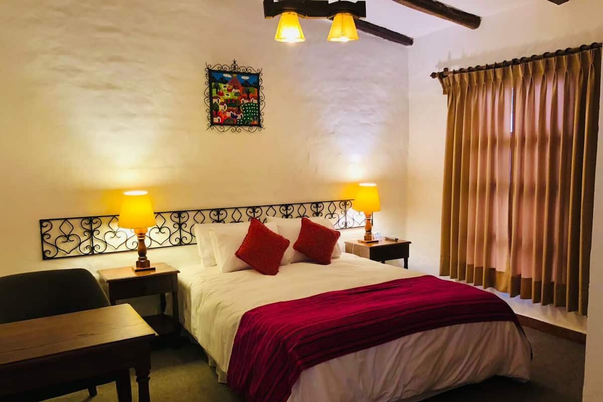 Una habitación de hotel con una cama, dos lámparas de noche, un escritorio y una silla.