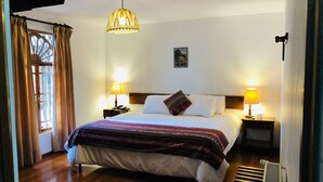 A neatly arranged hotel room with a large bed, two bedside lamps, a hanging light fixture, a small bedside table, and a radiator. - Hotel El Patio de Monterrey (Independencia)