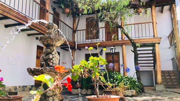 A courtyard with a stone fountain, potted plants, and a wooden staircase. - Hotel El Patio de Monterrey (Independencia)