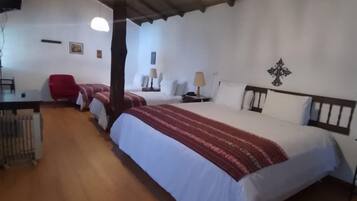 A room with a wooden floor, a bed with a red and white bedspread, a red chair, a desk with a lamp, and a wall-mounted cross decoration.