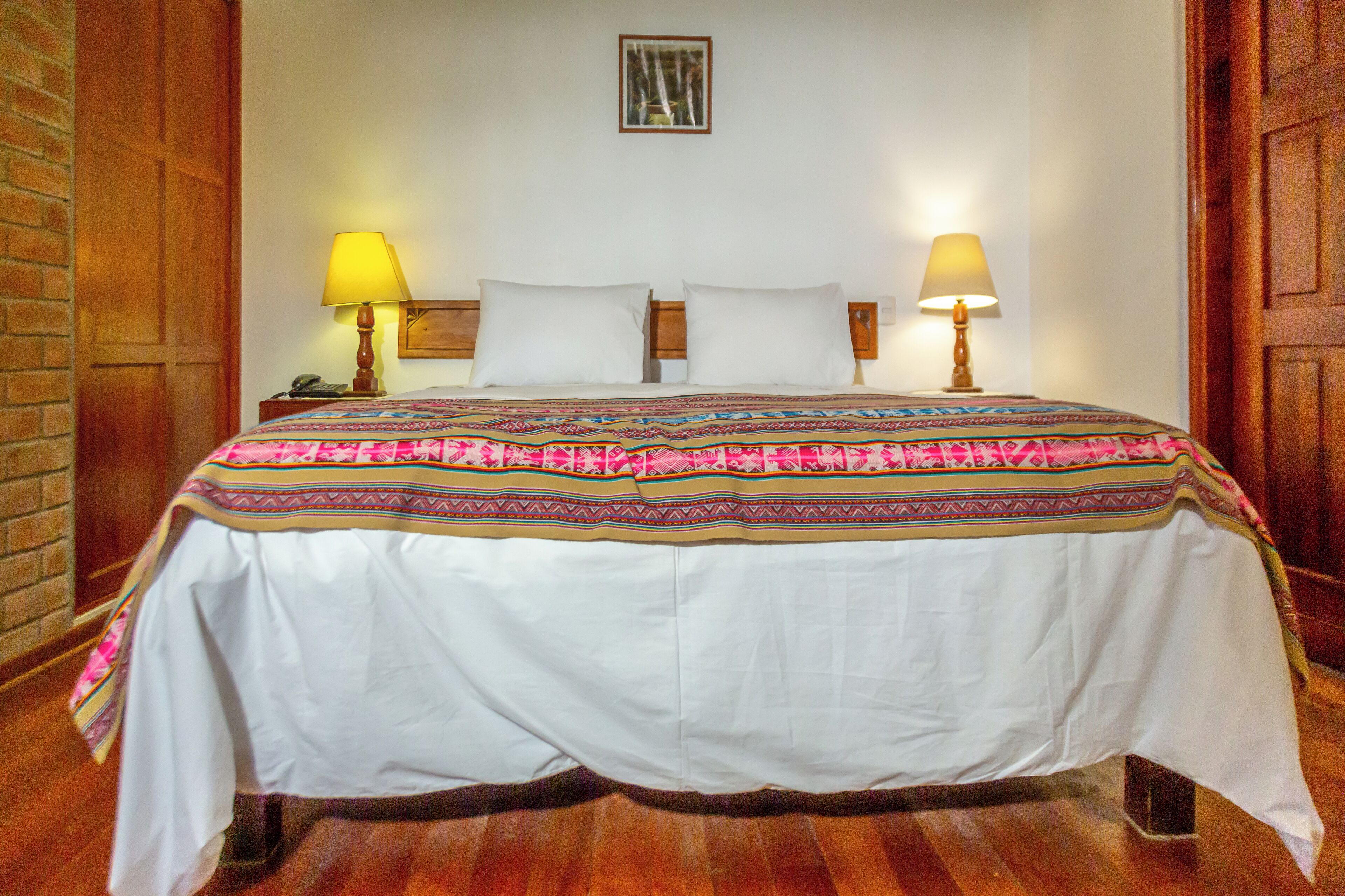 A neatly made bed with a patterned bedspread, two bedside lamps, and a wooden headboard.