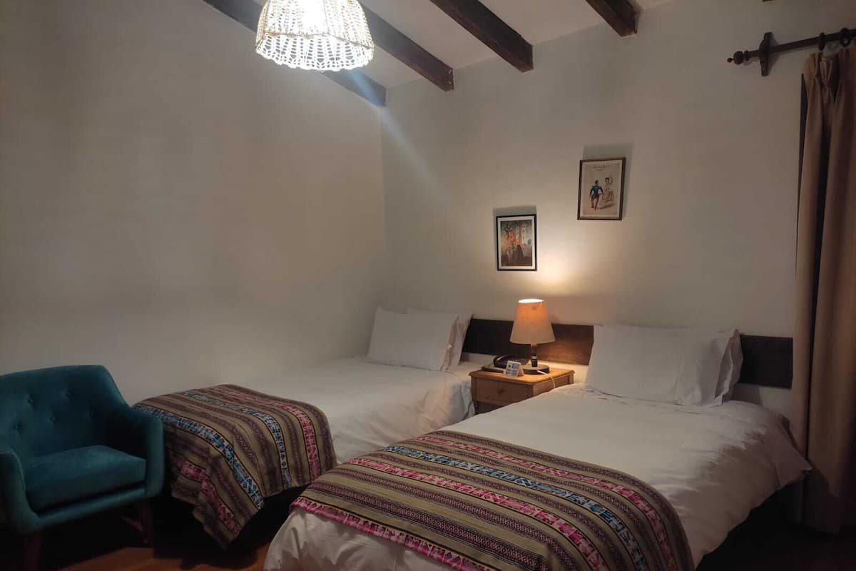 Una habitación con dos camas, una silla, una lámpara y una luz en el techo.