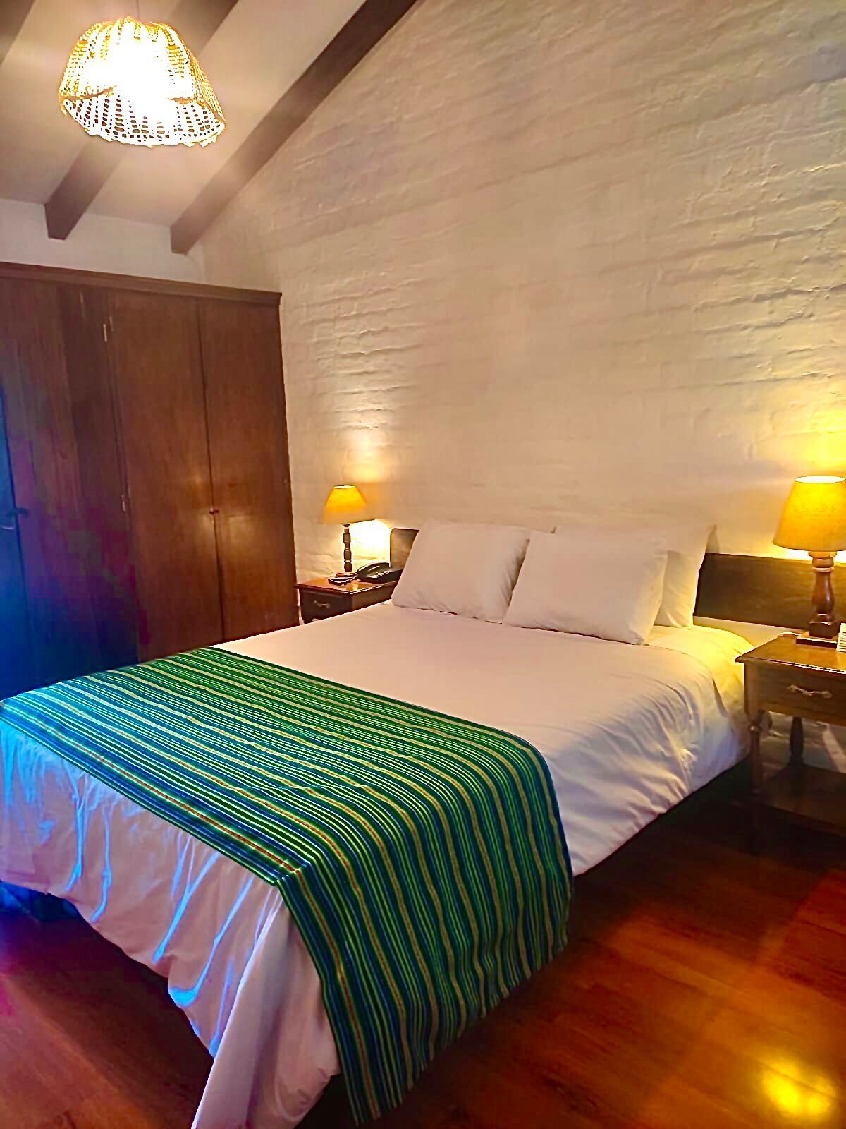 A bedroom with a large bed, two bedside tables with lamps, a wooden wardrobe, and a textured wall.