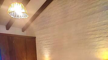 A bedroom with a large bed, two bedside tables with lamps, a wooden wardrobe, and a textured wall.