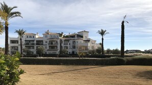A multi-story residential building with balconies, surrounded by a well-maintained lawn and palm trees. - Hacienda Riquelme Apartments (Murcia)