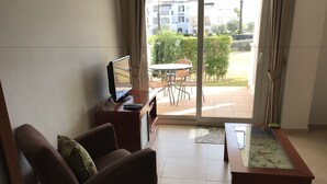 A living room with a sofa, a coffee table, and a TV on a wooden stand. There is a sliding glass door leading to an outdoor patio with a table and chairs. - Hacienda Riquelme Apartments (Murcia)