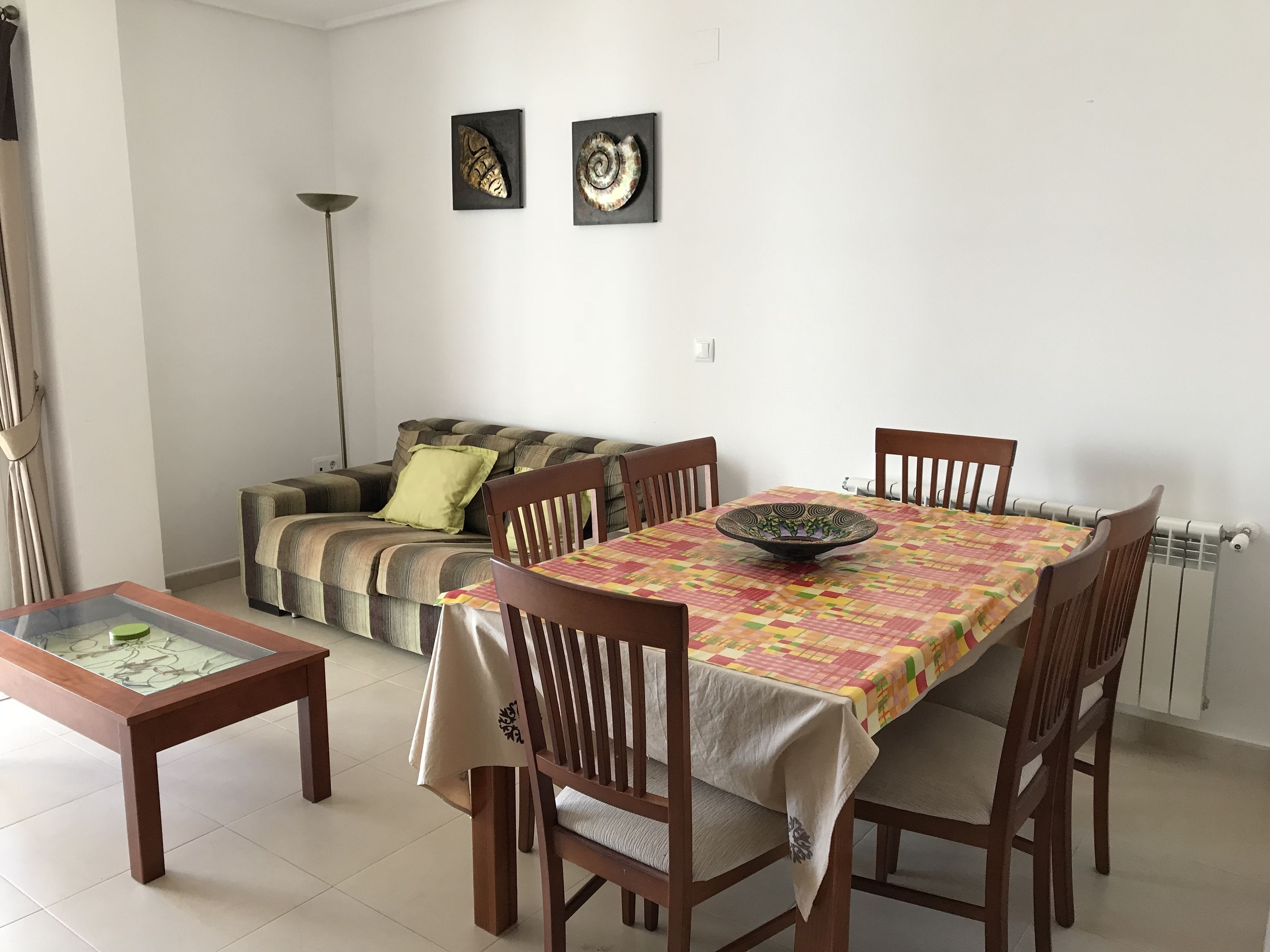 A dining area with a table set for four, a sofa, and a floor lamp.