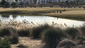 A golf course with a pond, grassy areas, and a hilly backdrop with white buildings. - Hacienda Riquelme Apartments (Murcia)