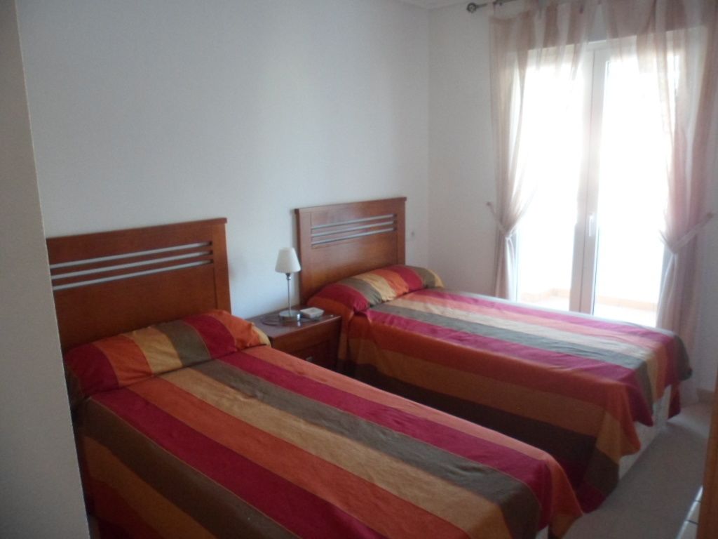 A room with two beds, each with a wooden headboard and striped bedding. There is a nightstand with a lamp between the beds.