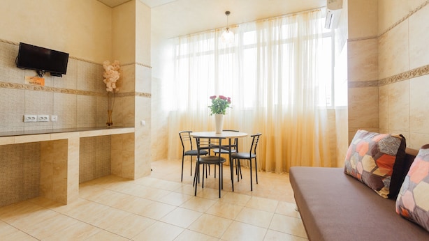 Una sala de estar moderna con un sofá, una mesa de comedor con sillas, un televisor de pantalla plana montado en la pared y una ventana con cortinas de gasa.