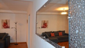 Un salón con un sofá gris oscuro, una lámpara de pie y dos cuadros con motivos florales rojos en la pared.