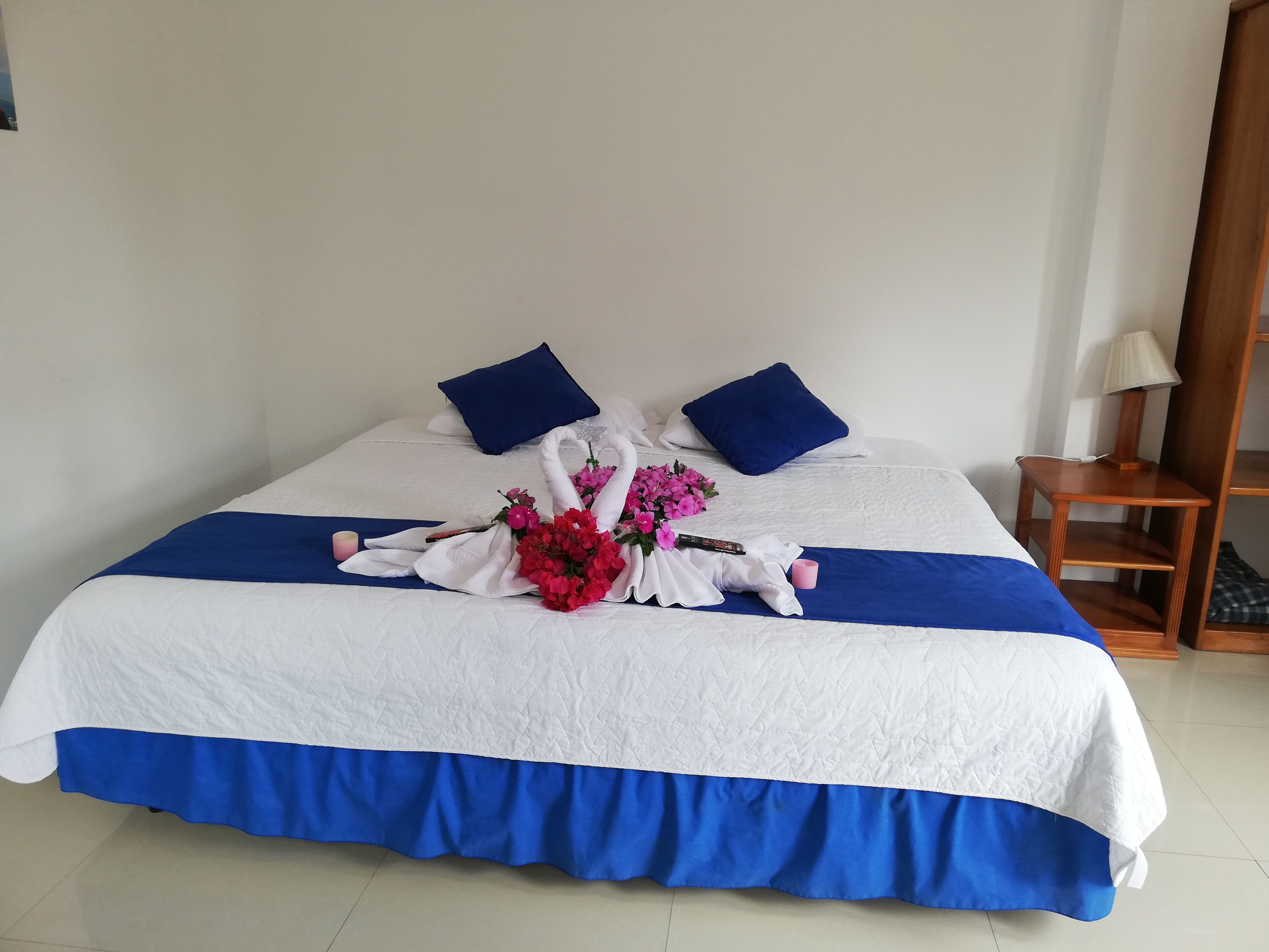Un lit bien fait, recouvert d’une couvre-lit bleue et blanche, avec deux oreillers bleus et un arrangement floral placé au centre.
