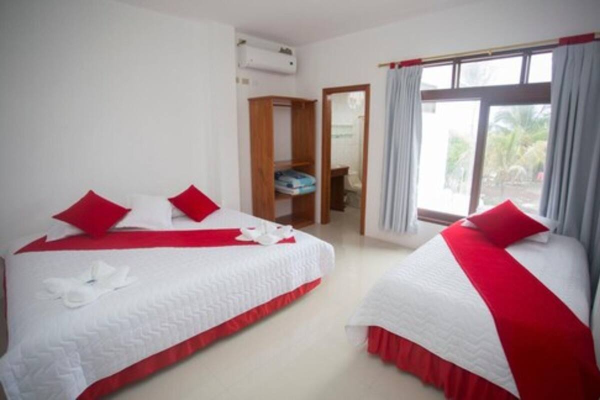 Une chambre d’hôtel avec deux lits, chacun agrémenté de draps rouges et blancs, une armoire en bois et une fenêtre avec des rideaux.