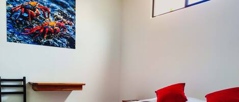 A hotel room with a checkered floor, a bed with red and white bedding, a red pillow, a white pillow, and a painting of a crab on the wall.