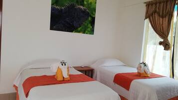 Habitación de hotel con dos camas, cada una con una colcha blanca y una manta roja. Hay una mesita con un control remoto y un marco de fotos en la pared sobre las camas.