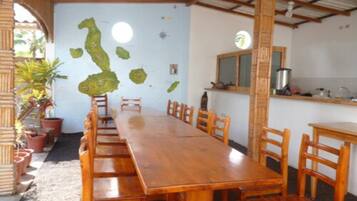 Une longue table à manger en bois, avec des chaises, un coin cuisine comprenant un évier et une cuisinière, et un mur orné d’une carte.