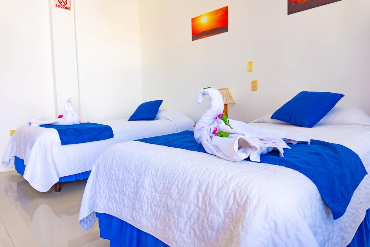 Une chambre d’hôtel avec deux lits, chacun recouvert d’une couvre-lit bleue et doté de draps blancs. On trouve sur les lits des serviettes en forme de cygnes, et un tableau représentant un coucher de soleil est accroché au mur.