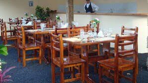 Un restaurante con mesas y sillas de madera, una barra con una persona detrás y plantas en macetas.