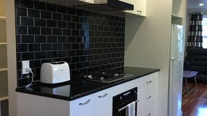 A compact kitchen with white cabinets, a black tiled backsplash, a built-in oven, and a white refrigerator. - Modern Home in Convenient Location (Auckland)