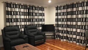 A living room with two armchairs, a wooden coffee table, a flat-screen TV, and black and white striped curtains. - Modern Home in Convenient Location (Auckland)