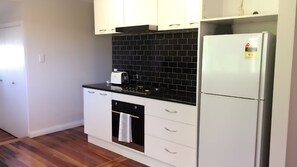 Una cocina compacta con armarios blancos, un salpicadero de baldosas negras, un refrigerador de acero inoxidable y un horno empotrado.